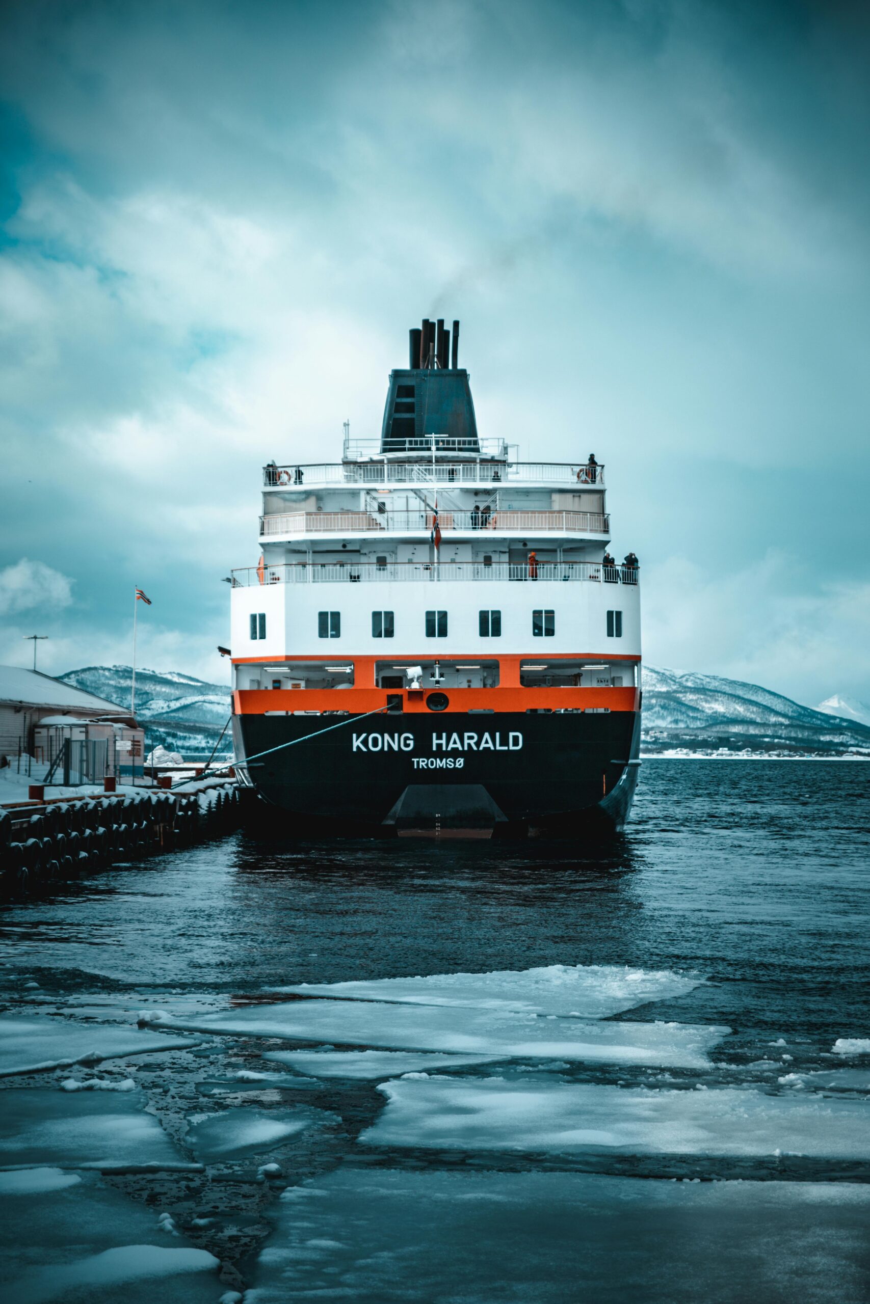 Majestic ferry Kong Harald docked at Finnsnes with icy waters and snowy mountains in view.